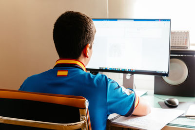 Rear view of man using mobile phone while sitting on chair