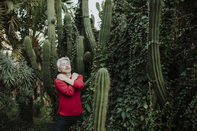 Mature man hugging self while standing in cactus garden