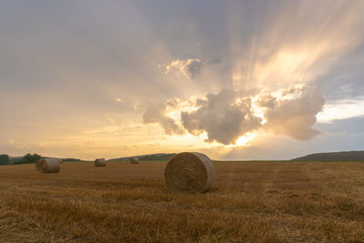 Hay bales on field against sky during sunset