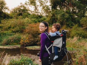 Smiling mother with cute son on back standing on forest