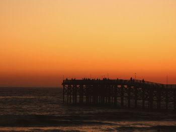 Silhouette pier over sea against orange sky