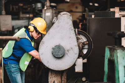 Full length of man holding hat standing in factory