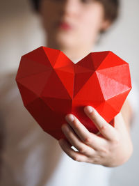 A nine-year-old boy holding a red origami heart in front of his face, white background