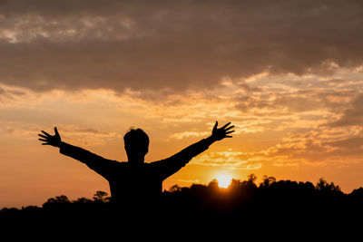 Silhouette man with arms outstretched standing against sky during sunset
