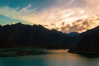 Scenic view of lake by mountains against sky during sunset