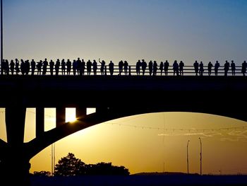Silhouette people on bridge against clear sky during sunset