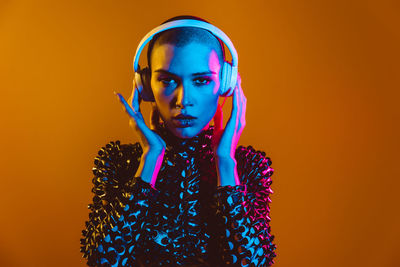 Young woman with shaved head wearing headphones against orange background