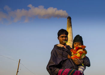 Father carrying daughter while standing against chimney and sky during sunset
