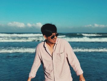 Man wearing sunglasses standing by sea against sky