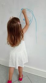 Rear view of girl writing on white wall at home