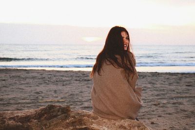 Portrait of smiling young woman sitting on driftwood at beach