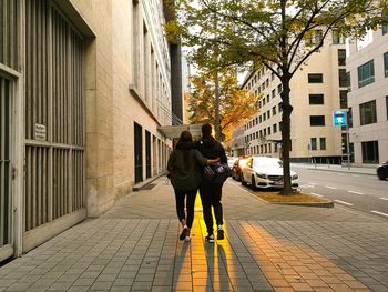 Rear view of friends with arm around while walking on sidewalk