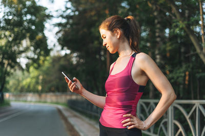 Young slim woman brunette in the sport clothes running and using mobile phone at park 