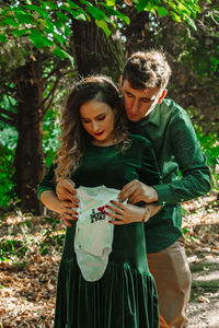 Pregnant woman with man holding baby clothing at forest