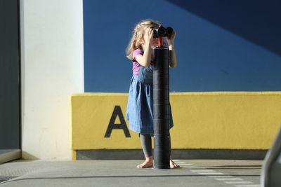 Girl using binoculars while standing against wall