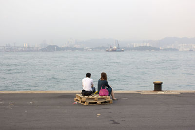 Rear view of couple sitting on sea against clear sky