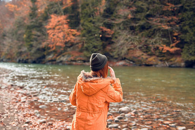 Rear view of woman standing by water during autumn