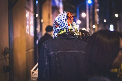 Rear view of woman standing against illuminated wall at night