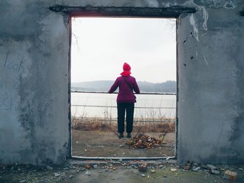 Rear view of woman standing by window against sky