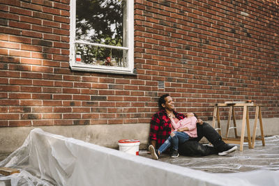 Cheerful girl sitting on father's lap against brick wall