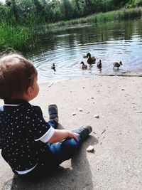 Rear view of boy sitting by swan in lake