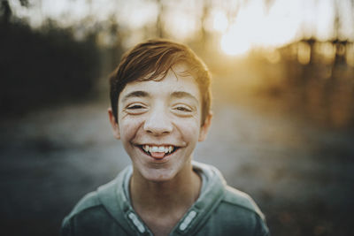 Close-up portrait of happy teenage boy standing outdoors during sunset