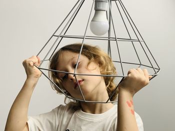 Depressed girl holding pendant light against white background