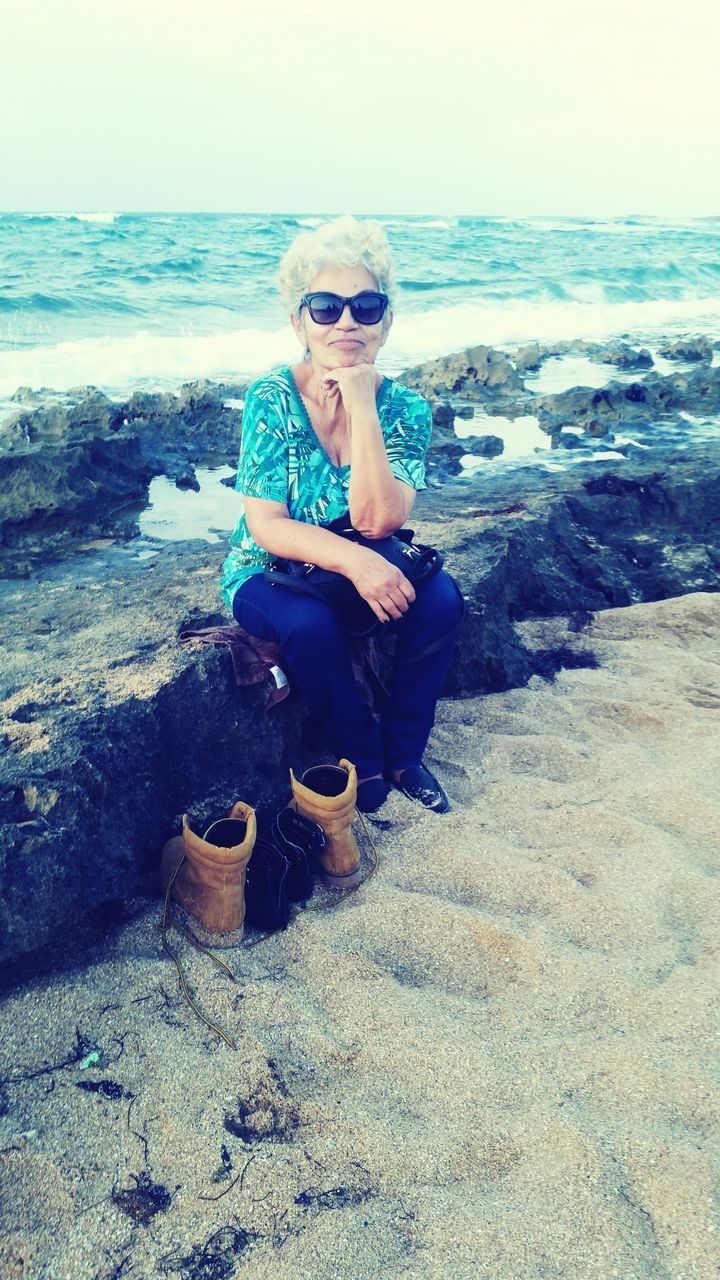 beach, sea, lifestyles, sand, young adult, leisure activity, shore, person, water, full length, vacations, portrait, sunglasses, looking at camera, sitting, young women, casual clothing, front view