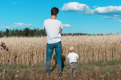 Rear view of father with son standing on field against sky