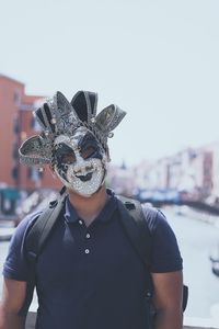 Portrait of man wearing venetian mask while standing against sky