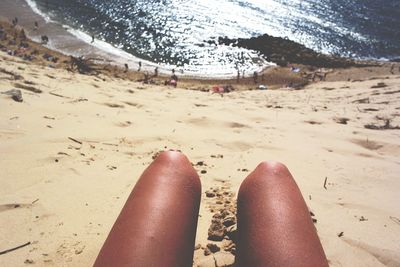 Low section of person relaxing on sand at beach