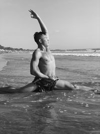 Shirtless man exercising in sea against sky