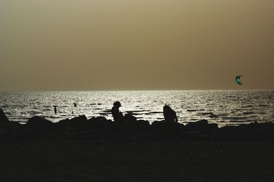 Silhouette people on beach against sky during sunset