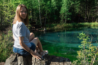 Woman sitting on rock by lake in forest