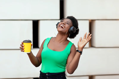 Happy african woman holding a coffee in a disposable cup, listening to the pleasant melody 