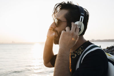 Man listening music against sea during sunset