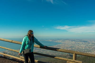 Mid adult woman standing by railing on observation point against blue sky during sunny day