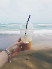 Cropped hand of woman holding disposable cup with drink at beach