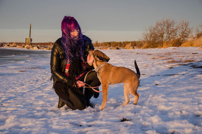 Woman with dog on snow field against sky