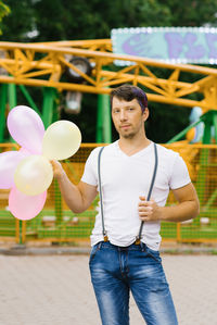 Funny guy is holding a bunch of balloons in his hands at an amusement park waiting for his beloved 