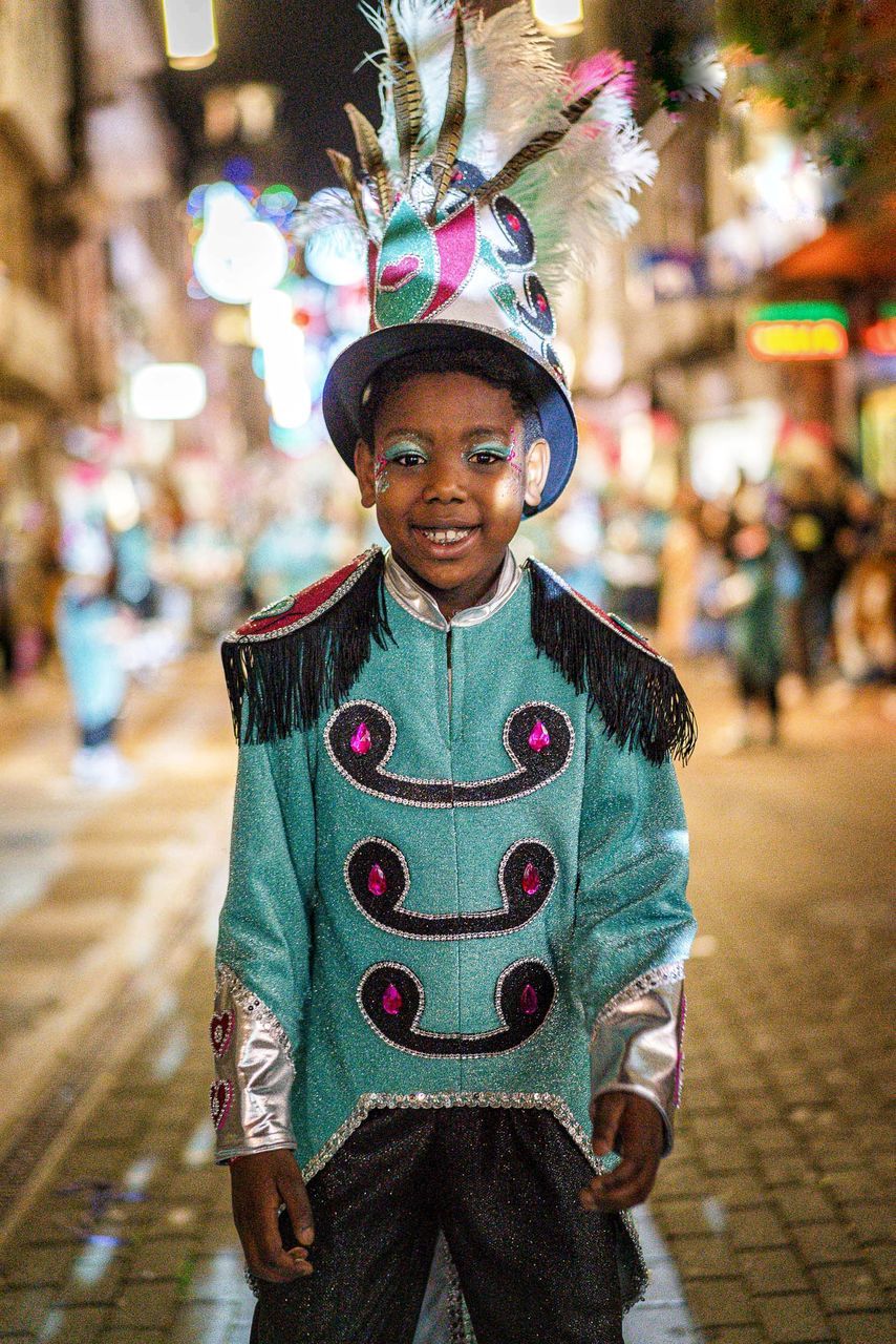 portrait, looking at camera, one person, smiling, front view, city, street, clothing, celebration, focus on foreground, childhood, men, standing, tradition, person, child, human face, happiness, emotion, architecture, outdoors, adult, lifestyles, arts culture and entertainment, headwear, costume, three quarter length, night