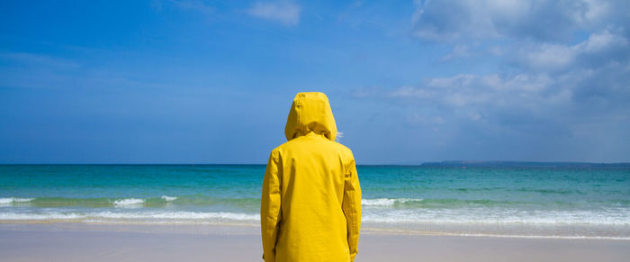 Rear view of woman standing at beach against sky