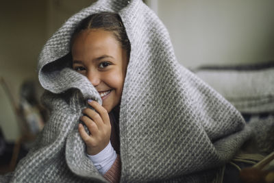Portrait of playful girl hiding under blanket at home