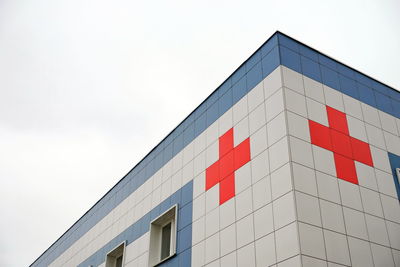 Medical symbol red cross on the cladding of the hospital building against the background of the sky.