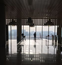 Silhouette people walking in airport seen through glass window