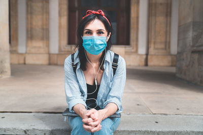 Portrait of young woman sitting against building