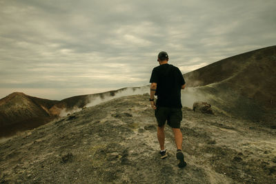 Rear view of man standing on mountain against sky