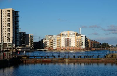 Buildings by river against blue sky