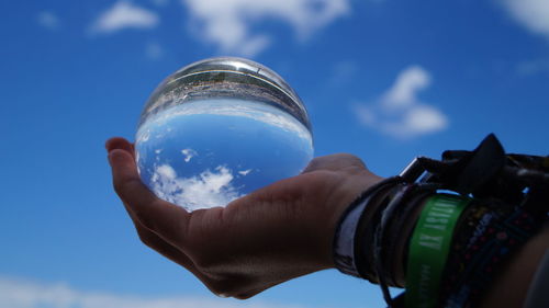 Close-up of hand holding camera against sky