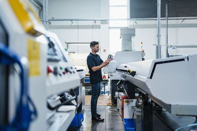 Mature male technician examining machine part while standing in industry